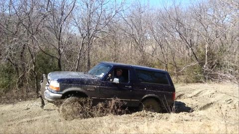 1995 Ford Bronco - Ford Bronco navigating a muddy trail with trees in the background.