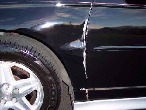 2002 Chevrolet Monte Carlo - Damage is visible on the fender and door seam of a black car, with rust appearing at the bottom.