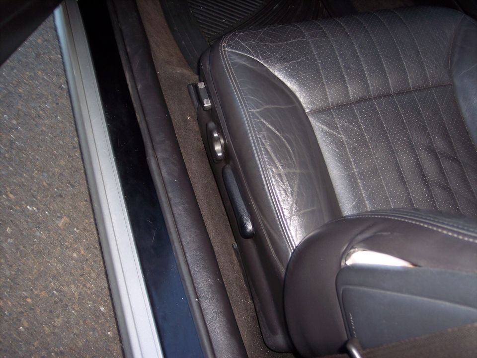 Close-up of worn black leather driver's seat with visible stitching and perforation detail