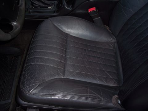 2002 Chevrolet Monte Carlo - Interior view of a worn black leather car seat, including the steering wheel and gear shifter.