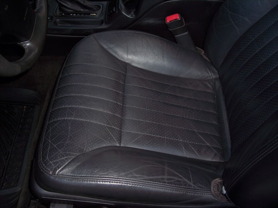 Black leather driver's seat with perforated inserts and visible wear, showing part of the steering wheel and center console