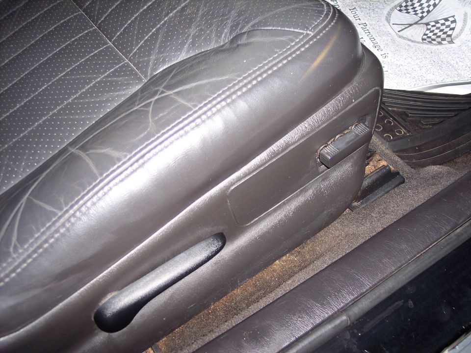 Close-up of a dark leather car seat with visible wear and adjustment levers