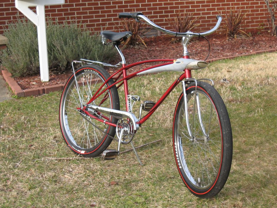 Red cruiser bicycle with chrome handlebars and fenders, parked on grass