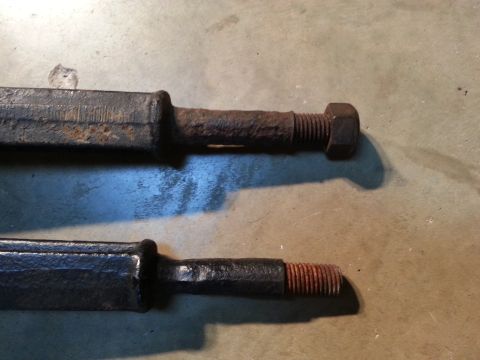 1995 Ford Bronco - Close-up of two rusty metal rods with threaded ends, one secured by a nut.
