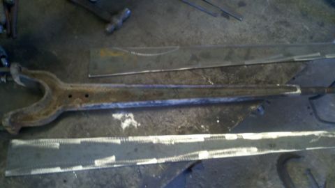 1996 Ford Bronco - A rusty suspension part rests on a workbench next to metal plates.