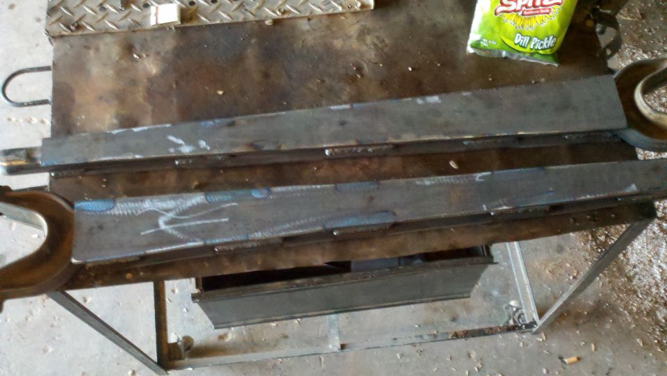 Welded metal parts on a workbench with a bag of dill pickle chips