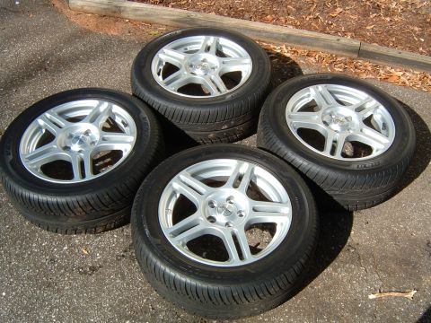 1997 Ford Taurus - Four alloy wheels with tires are displayed on a paved surface, with a wooden beam visible in the background.