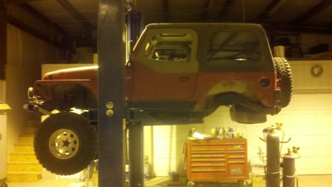 1996 Ford Bronco - A red Jeep Wrangler is elevated on a lift in a workshop, showing its side profile and missing its front bumper.