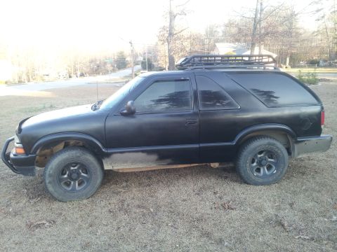 1986 Ford Bronco - Side view of a black Chevrolet Blazer with a roof rack, parked outdoors.