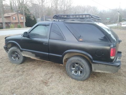 1986 Ford Bronco - This black SUV is parked on a dry, grassy area with houses in the background.