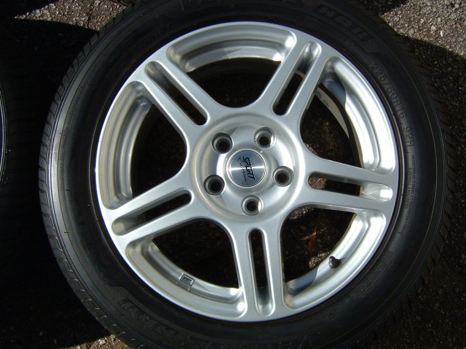 Silver 5-spoke wheel with black tire and 'SPORT' center cap