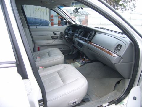 2003 Ford Crown Victoria - The interior of a 2003 Ford Crown Victoria, light grey leather seats and a grey dashboard with visible wiring.