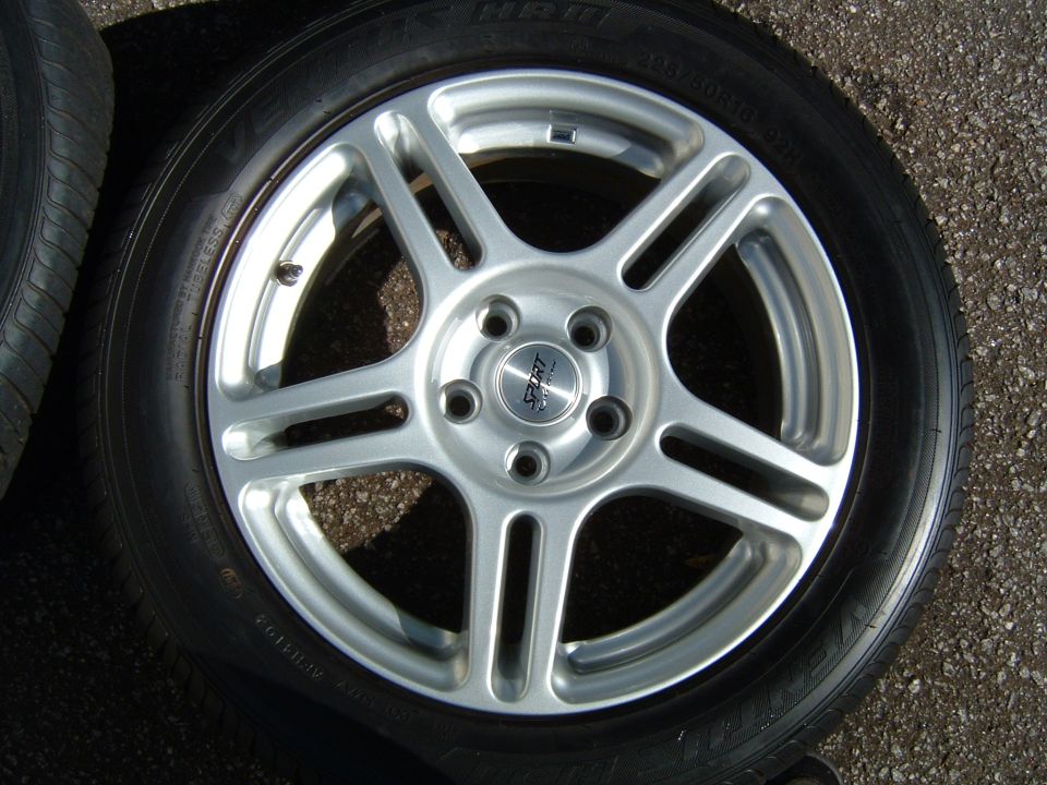 Aftermarket 5-spoke wheel with 'SPORT' center cap and tire