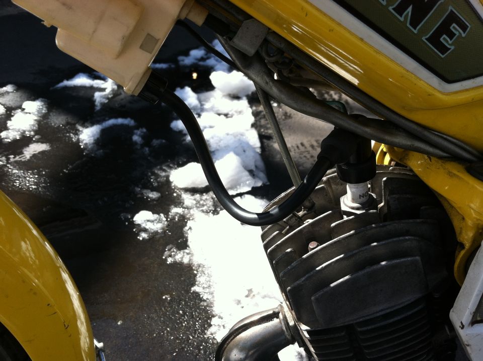 Close-up of a moped engine cylinder and spark plug, with a yellow body panel and snow on the ground
