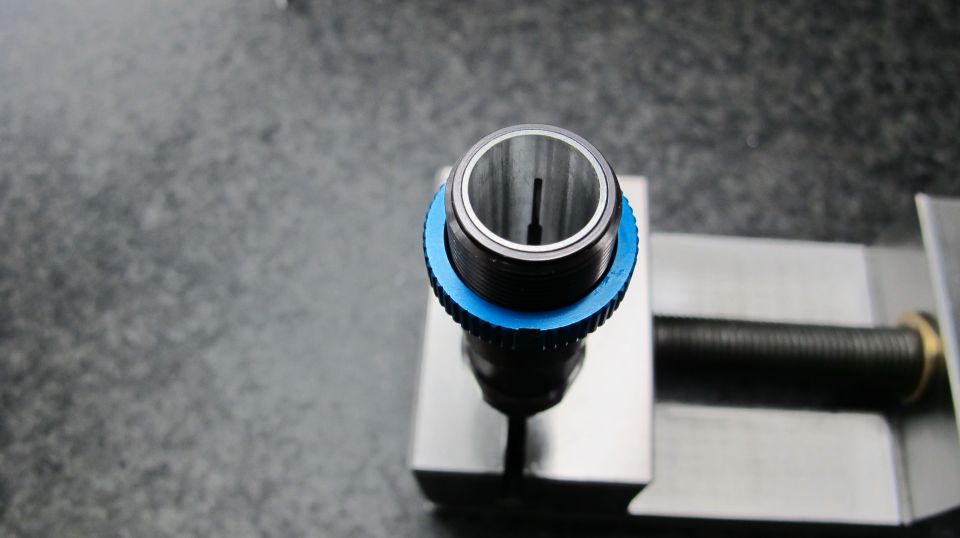 Close-up of a shock absorber component with a blue adjustment ring, held in a metal vise