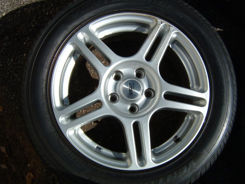 Close-up of a silver 5-spoke alloy wheel with a 'Sport' center cap and tire