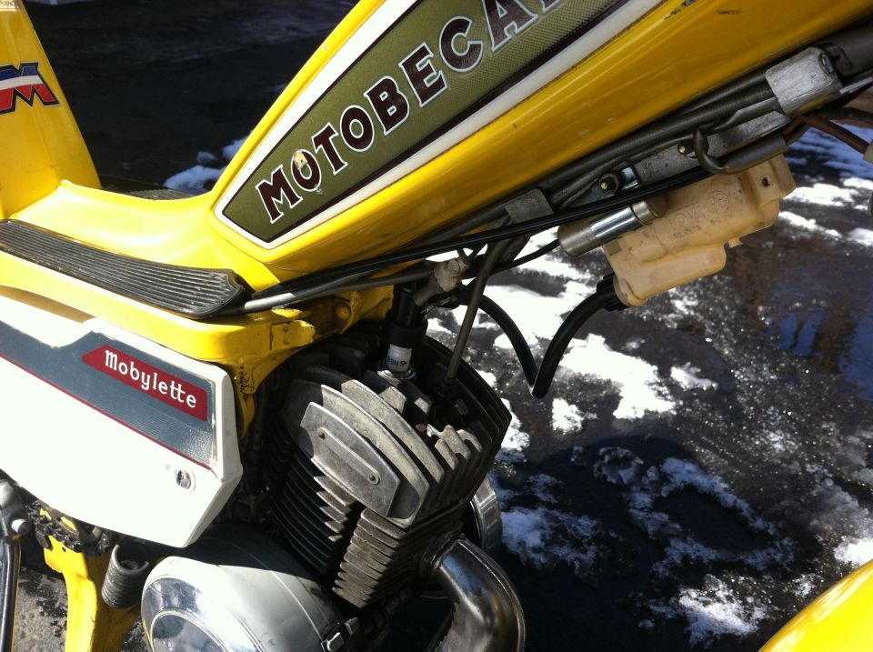 Yellow Motobecane Mobylette moped engine and fuel tank with text.