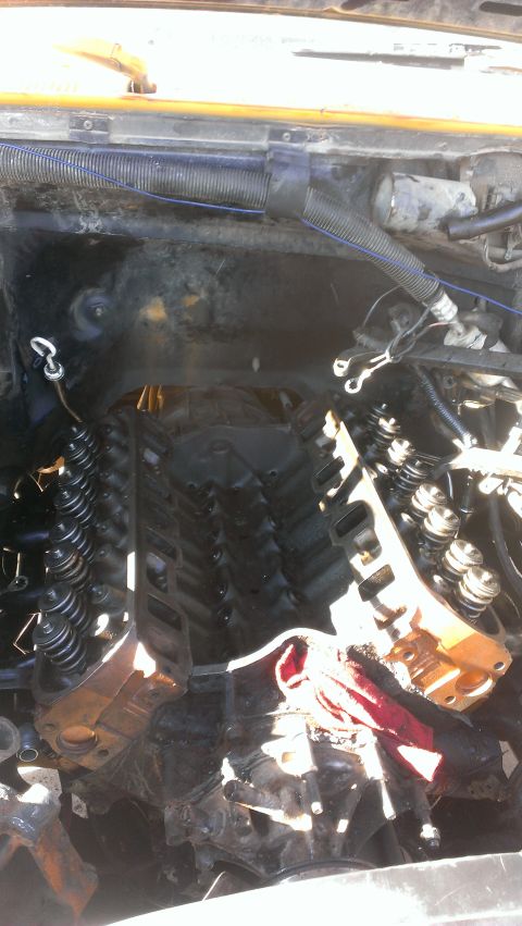 1990 Ford Bronco - The image shows the engine bay of a vehicle, with the intake manifold removed, revealing the cylinder heads and valve train components. A r…