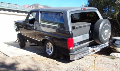 1996 Ford Bronco - A black Ford Bronco full-size SUV viewed from the rear three-quarter left side, with a rear-mounted spare tire cover reading 'Ford Bronco'…