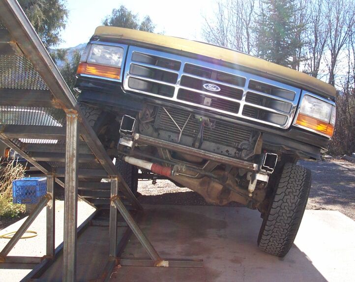 Green Ford truck front end raised on ramps showing underside and front axle outdoors
