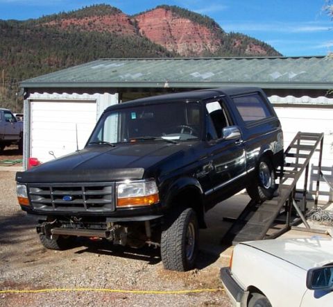 1996 Ford Bronco - A black 1990s Ford Bronco full-size SUV parked on gravel with its front bumper removed, exposing a winch and mounting hardware. It sits at…