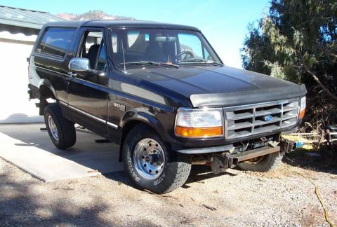 1996 Ford Bronco - A black Ford Bronco full-size SUV shown from the front three-quarter angle, with chrome grille bearing the Ford oval, amber turn signals, a…