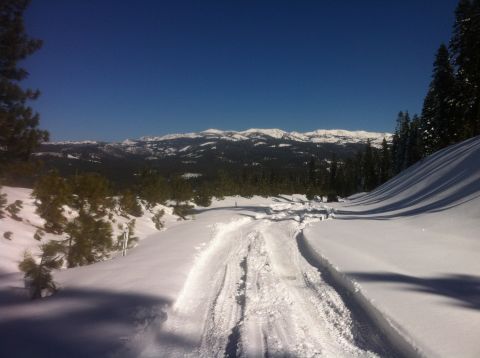 1989 Ford Bronco - Tire tracks mark a path through a snowy mountain landscape with distant peaks.