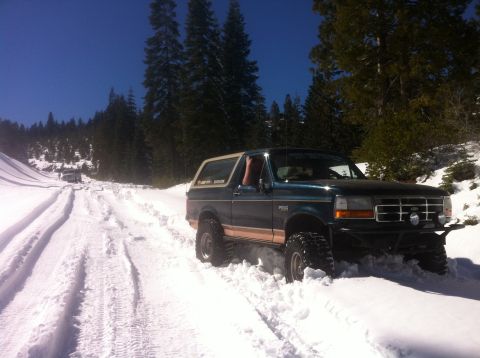 1989 Ford Bronco - A Ford Bronco navigates a snow-covered road, leaving tracks behind as it moves forward.