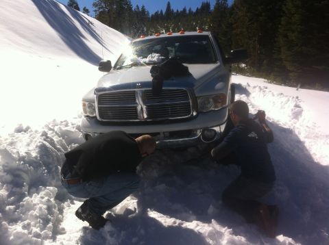 1989 Ford Bronco - A white Dodge Ram pickup truck is stuck in the snow, with two men inspecting the front.
