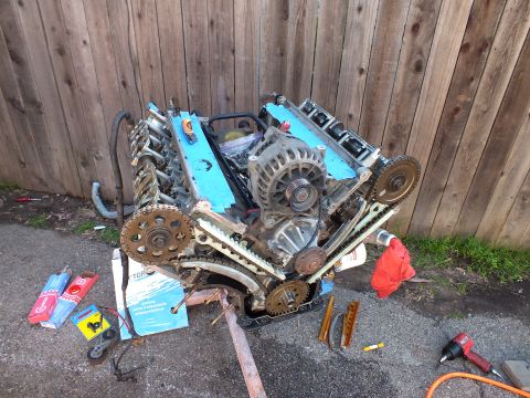2003 Ford Crown Victoria - Front of a DOHC V6 with timing chains and gears exposed, gasket boxes and tools scattered on pavement.