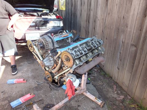 2003 Ford Crown Victoria - Engine pulled and mounted on a stand next to a pickup with its hood raised, person standing at left.