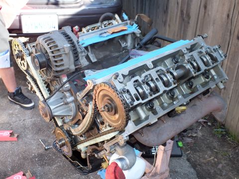 2003 Ford Crown Victoria - Three-quarter view of a DOHC V6 with alternator and timing chains exposed, vehicle and gasket box in background.