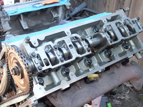 2003 Ford Crown Victoria - Camshaft and valves visible on an aluminum cylinder head, timing chain sprocket and exhaust manifold alongside.