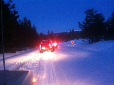 1989 Ford Bronco - Two vehicles travel on a snow-covered road under a dark blue sky.