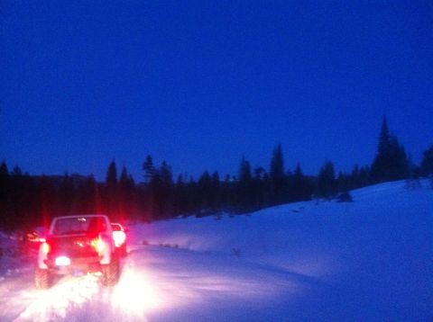 1989 Ford Bronco - Two vehicles drive on a snow-covered road under a deep blue twilight sky, with trees silhouetted in the background.