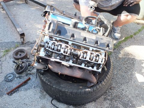 2003 Ford Crown Victoria - Engine sitting on a tire with cam covers off and chains visible, pulleys and tools spread on the ground.
