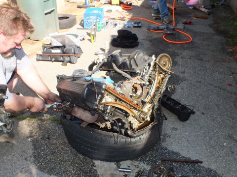 2003 Ford Crown Victoria - Mechanic removing a component from an engine balanced on a tire, intake and tools laid out on pavement.