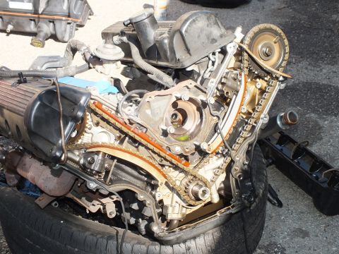 2003 Ford Crown Victoria - Close view of the timing case with chains, guides and crank sprocket exposed on an engine resting on a tire.