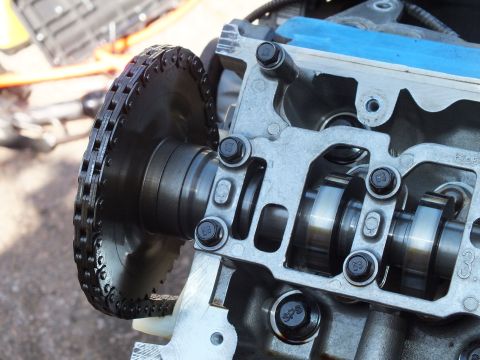 2003 Ford Crown Victoria - Macro of a cam sprocket wrapped in chain alongside camshaft journals on a V6 cylinder head.