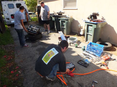 2003 Ford Crown Victoria - Driveway engine teardown with one man kneeling over parts and tools spread across the pavement.