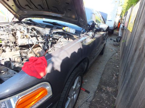 2003 Ford Crown Victoria - Dark Ford sedan parked along a wood fence with hood up and a red rag on the fender.
