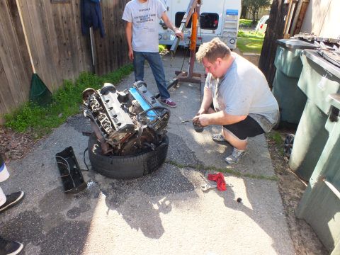 2003 Ford Crown Victoria - Mechanic working a hand tool on an engine propped on a tire during a backyard teardown.