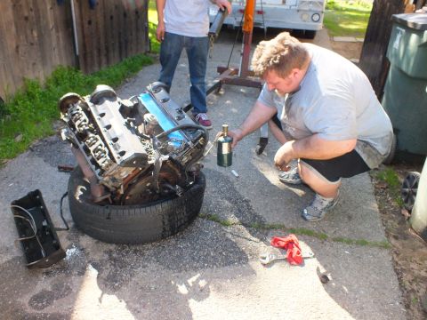 2003 Ford Crown Victoria - Mechanic positioning a brass torch near an engine set on a tire during a driveway rebuild.