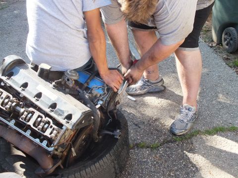 2003 Ford Crown Victoria - Close work on a removed engine with one person turning a wrench at the rear of the block.