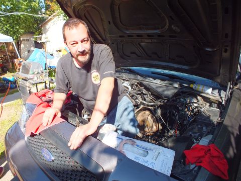 2003 Ford Crown Victoria - Man resting on the front of a gray Ford during engine work, exposed bay and red rags visible.