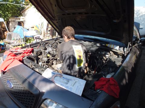 2003 Ford Crown Victoria - Mechanic reaching into a gray Ford engine bay with red rags and paperwork on the fender.