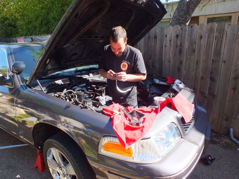 2003 Ford Crown Victoria - Close work at the open engine bay of a gray sedan beside a wood fence, tools on a red rag.