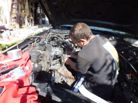 2003 Ford Crown Victoria - Close-up of hands working an exposed engine block inside a sedan bay, red rag on the fender.