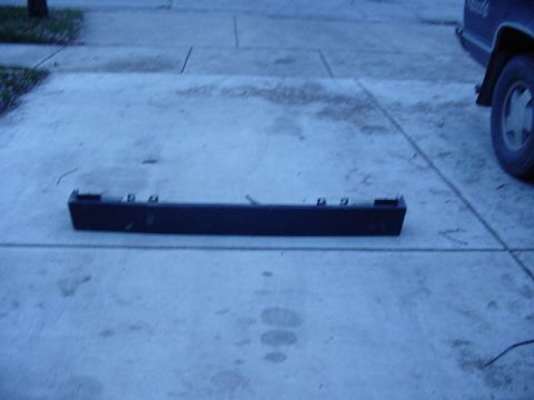 1992 Ford Bronco - A black plastic bumper trim piece lies on a concrete driveway.