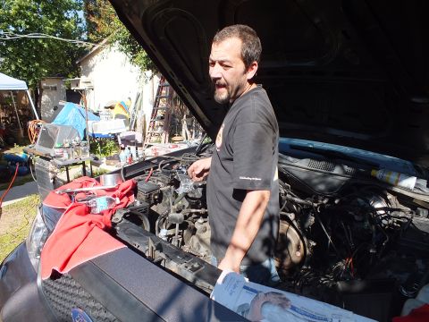 2003 Ford Crown Victoria - Man pauses over the open engine bay of a dark sedan, Ford-marked rag draped on the fender.